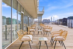 A rooftop terrace with wicker chairs and tables, large windows offering city views, and a glass railing. - Radisson Blu Bordeaux (Bordeaux)