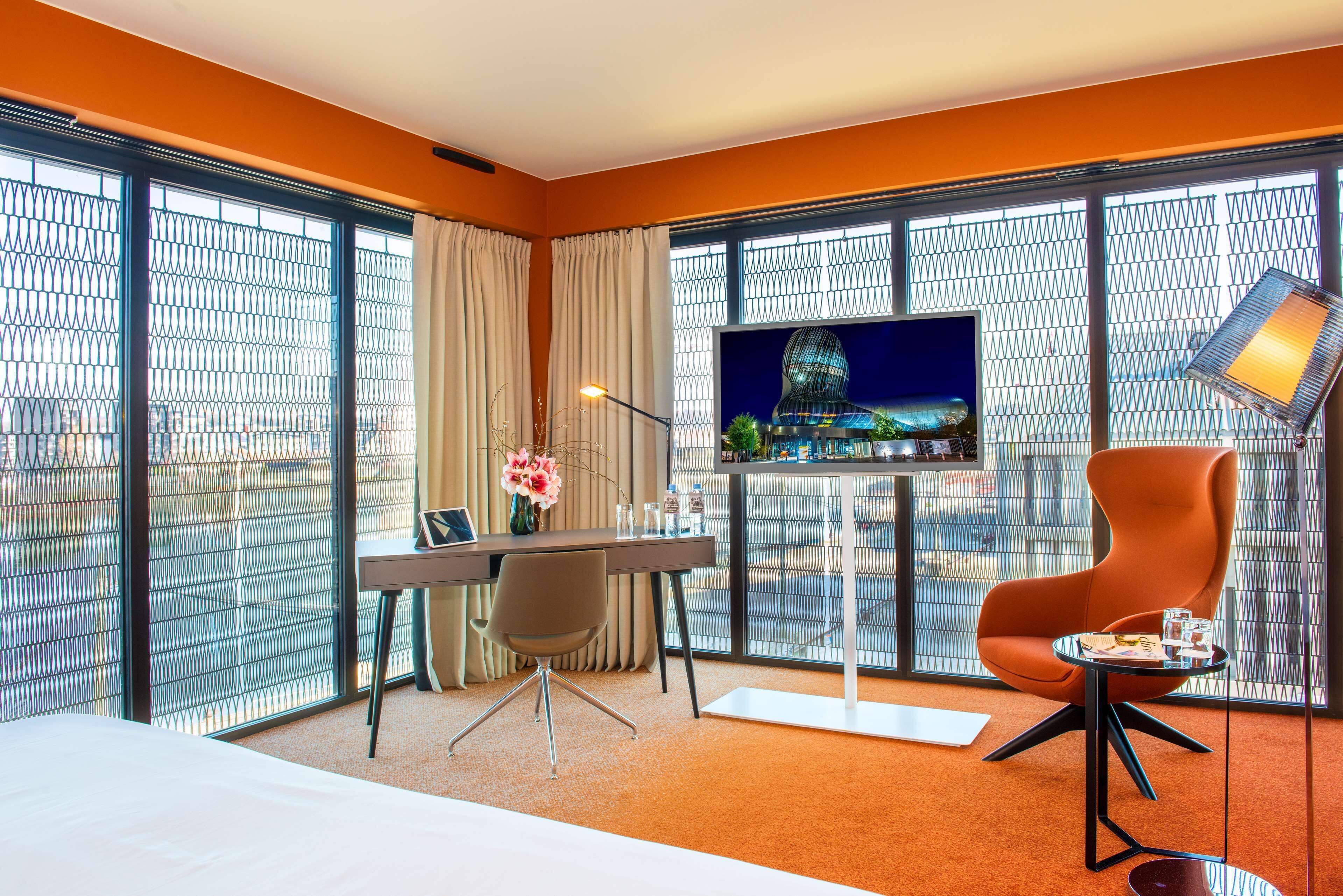 Una habitación de hotel con una cama, un escritorio con computadora, televisor y una silla.