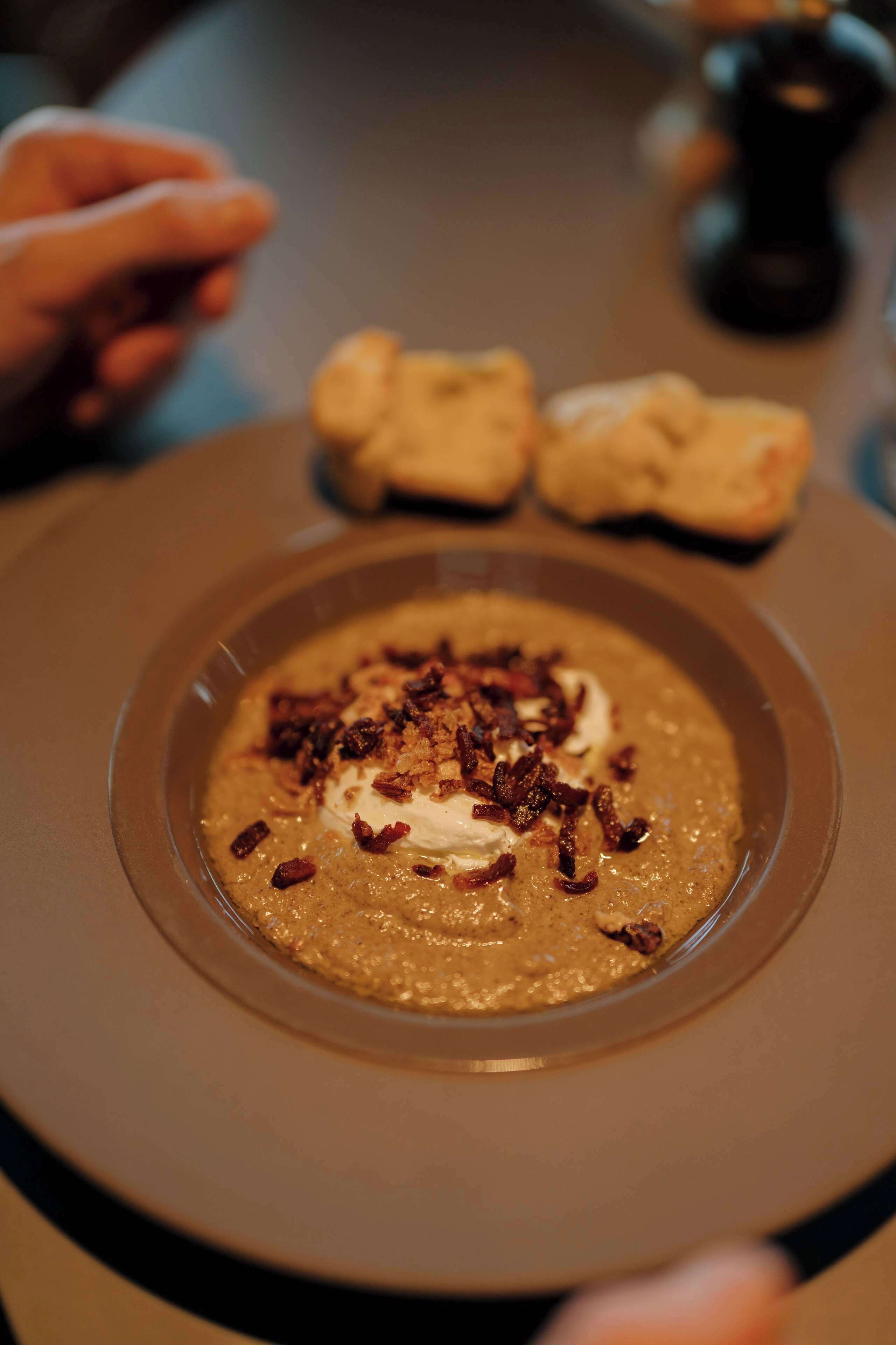 A bowl of soup with a creamy texture, garnished with a dollop of cream and crispy toppings, served on a brown plate.