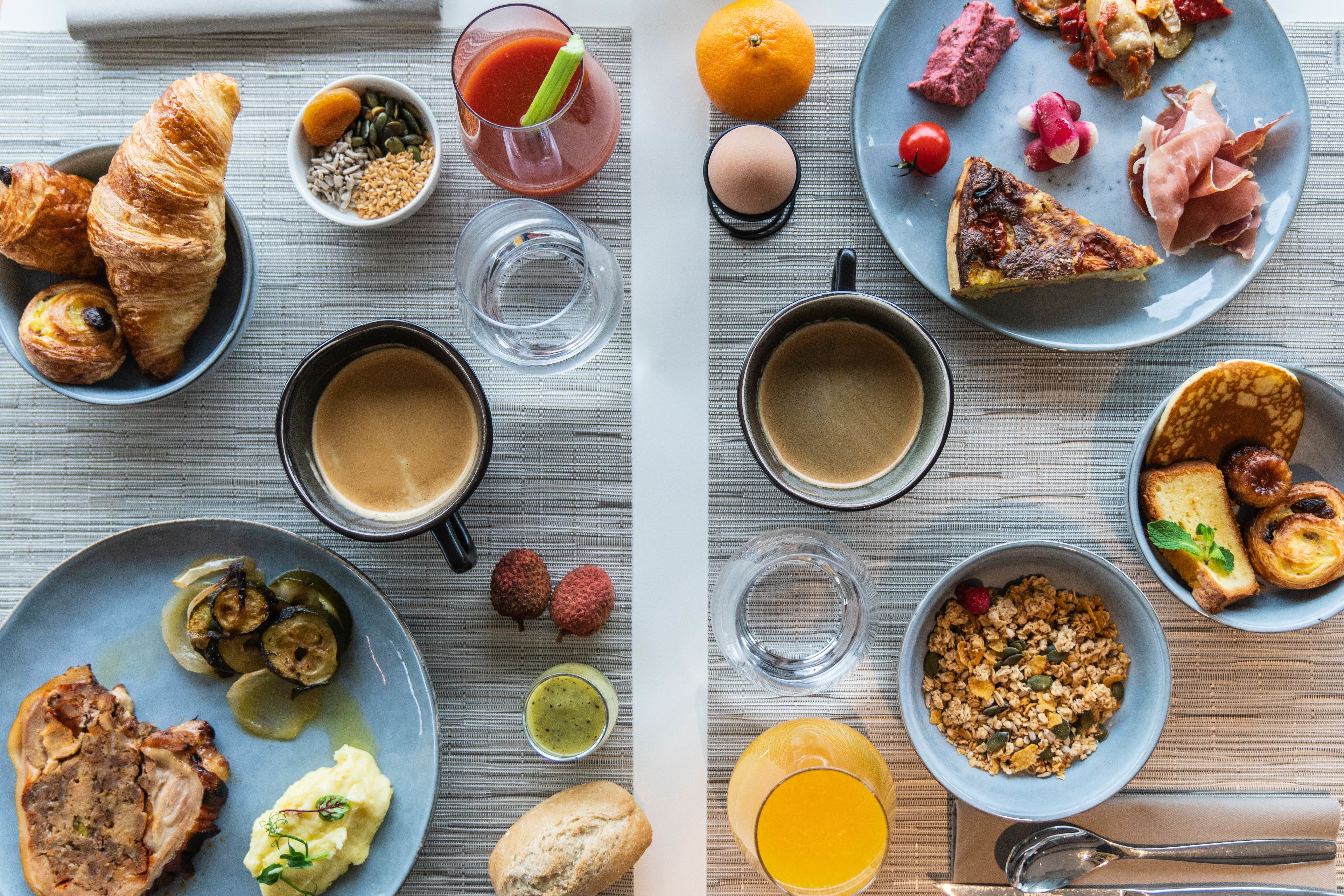 A breakfast spread with croissants, eggs, meats, and various fruits on a table.