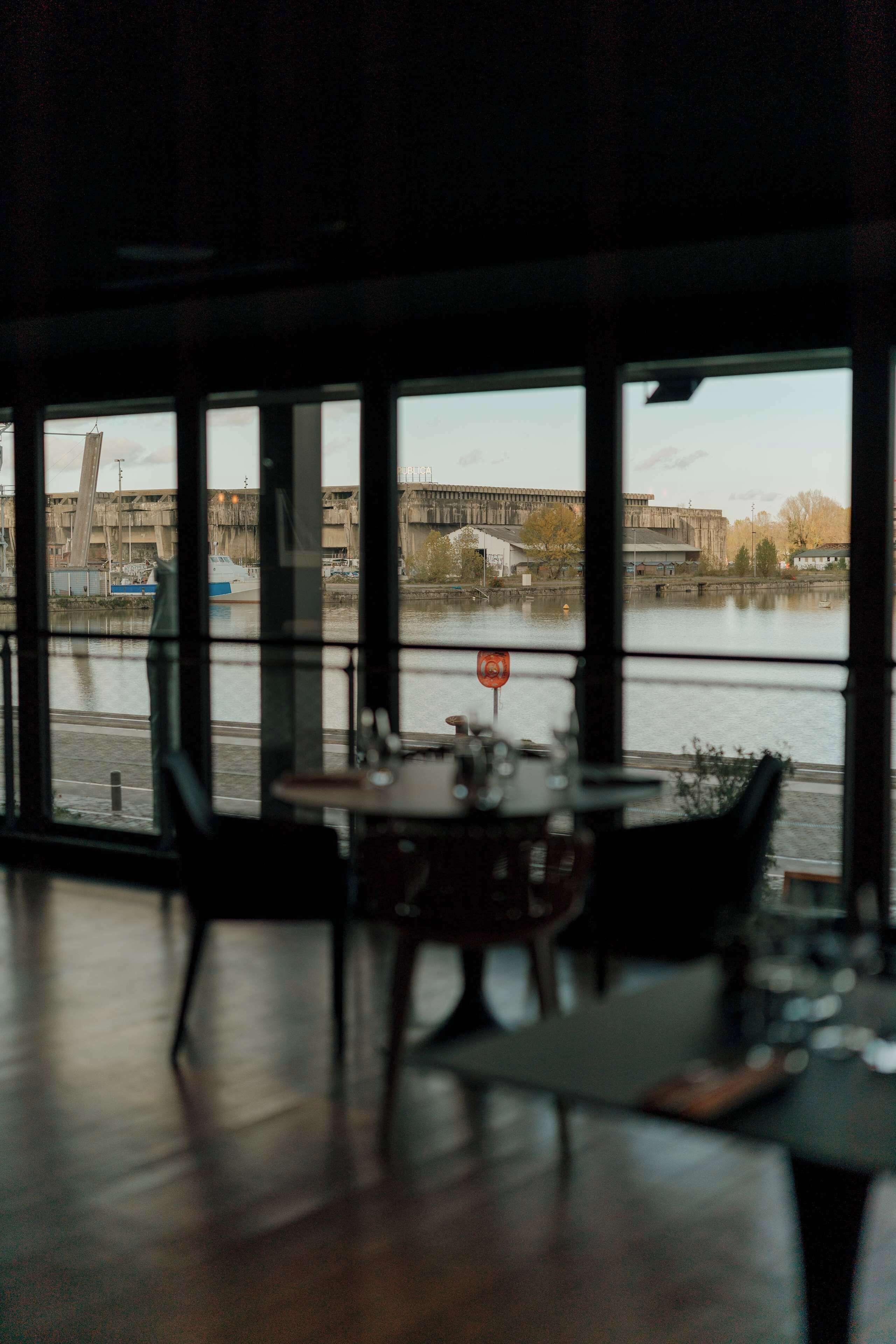 A dining area with a view of a river and industrial buildings.