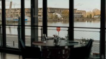 A dining area with a view of a river and industrial buildings.