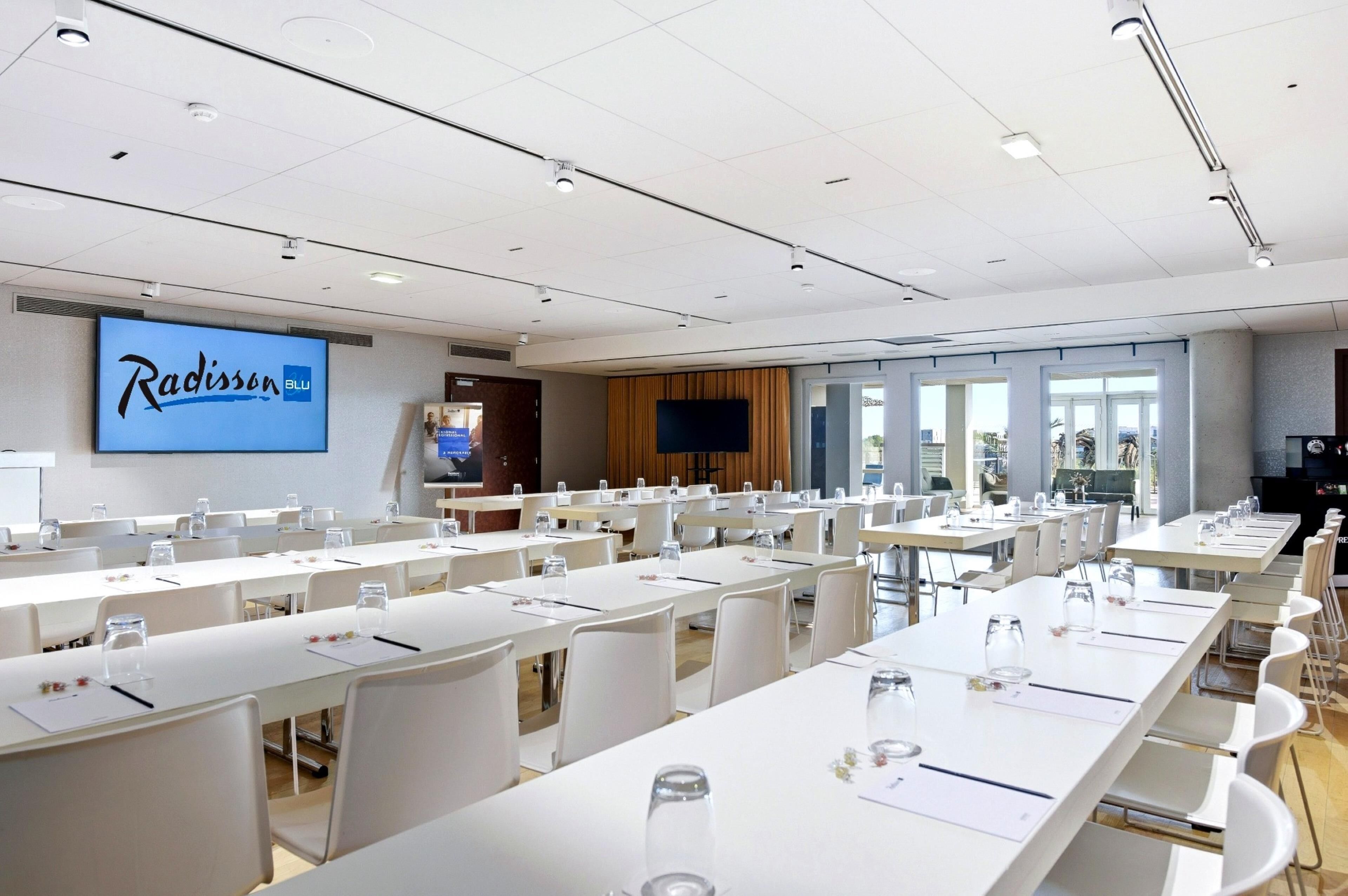 Une salle de conférence avec de longues tables, des chaises blanches et un panneau Radisson Blu sur le mur.