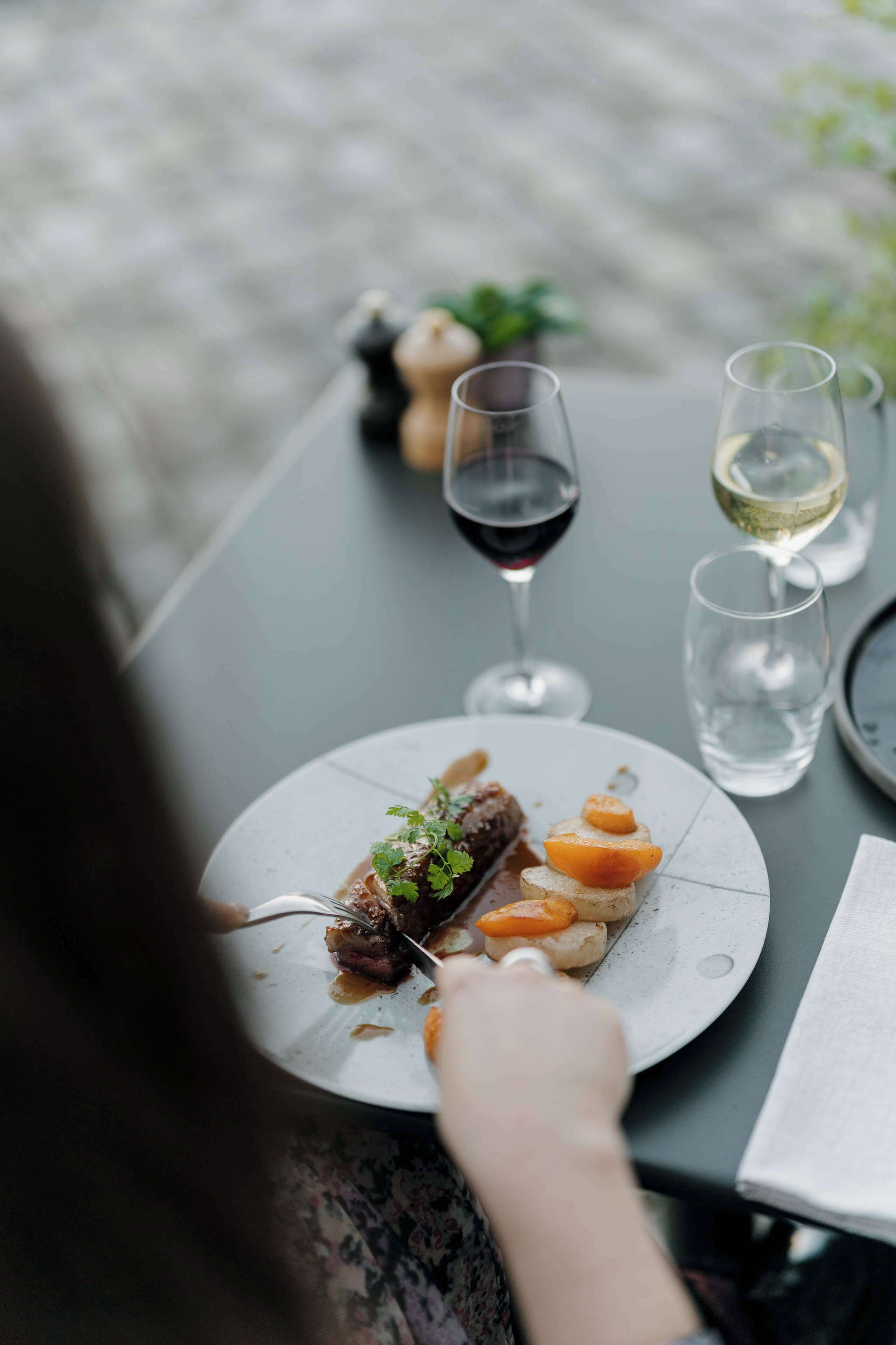 A dining table with a plate of food, two glasses of wine, and a person eating.
