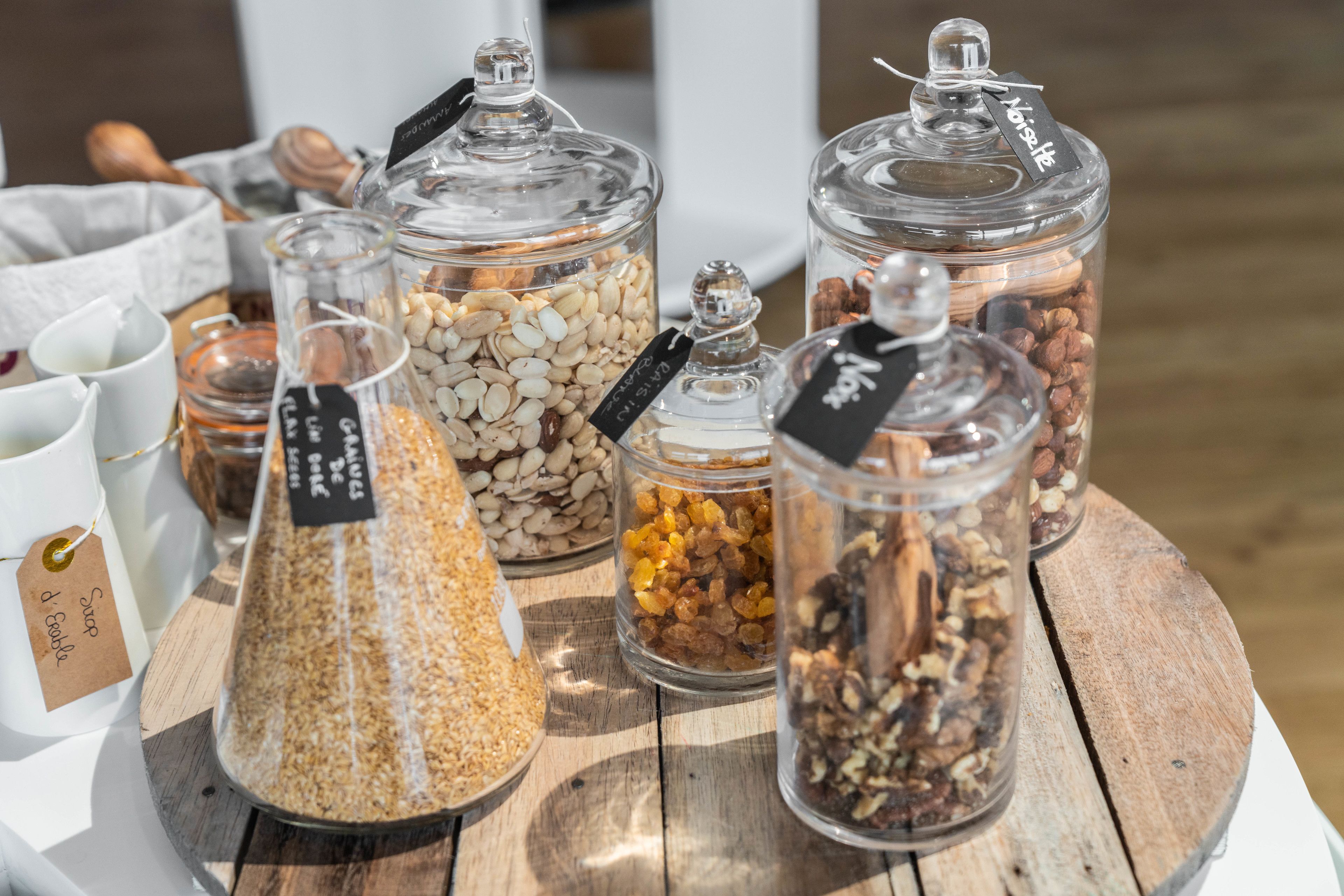A wooden table with various glass jars containing different types of grains and seeds, each labeled with tags.