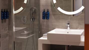 A modern bathroom with a glass-enclosed shower, a white sink, and two round mirrors with illuminated frames.