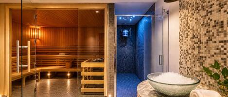 Ein modernes Spa mit einer Holzsauna, einer gläsernen Duschkabine und einer Schale Salz auf einer gefliesten Ablagefläche.
