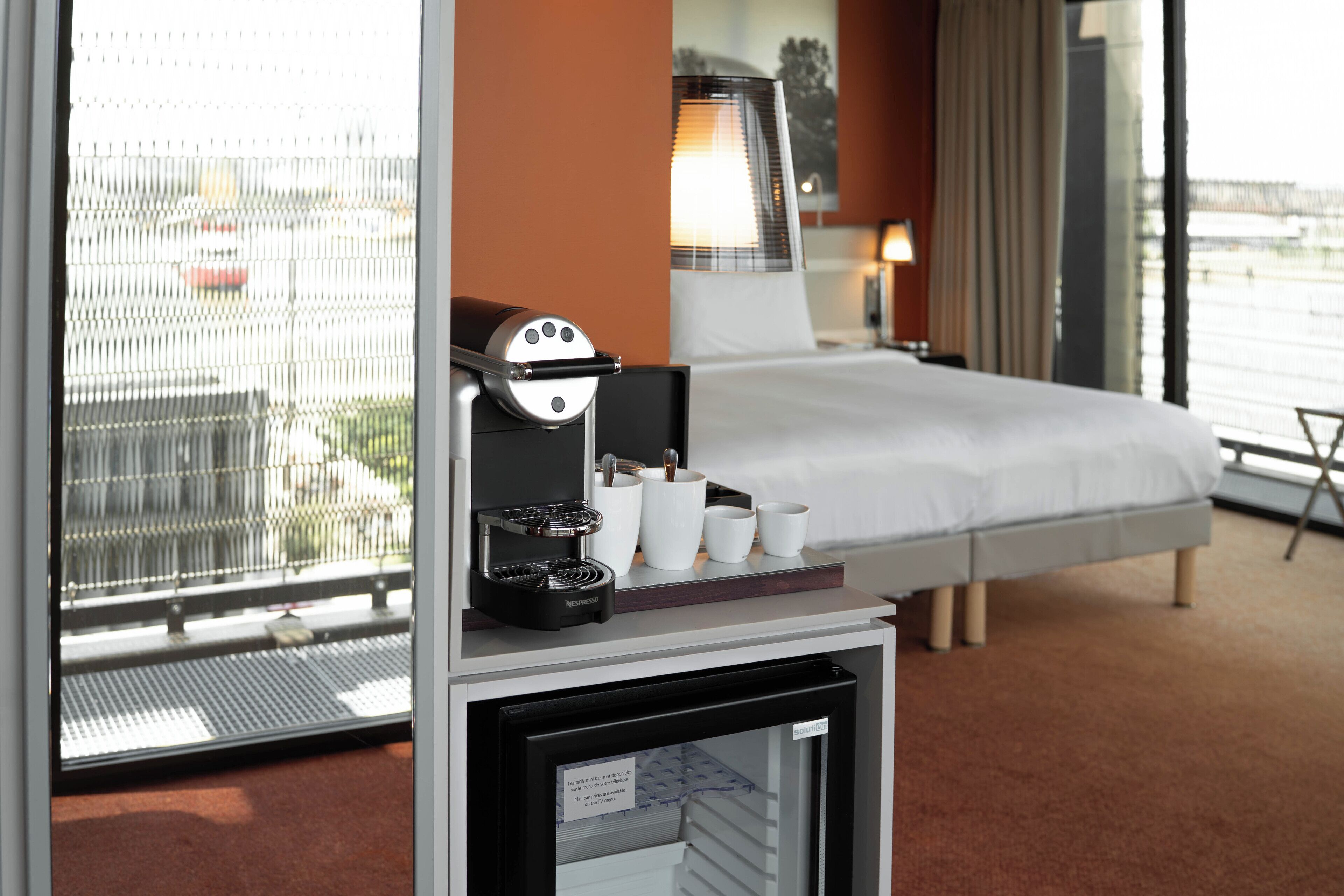 A hotel room with a bed, a coffee machine, and a mini fridge.