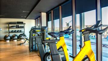Un gimnasio con bicicletas estáticas, una máquina de pesas y un estante con balones medicinales.