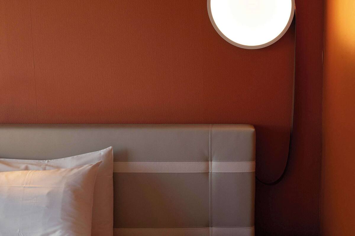 Une chambre d’hôtel avec un lit, une table de chevet et un luminaire rond fixé au mur.