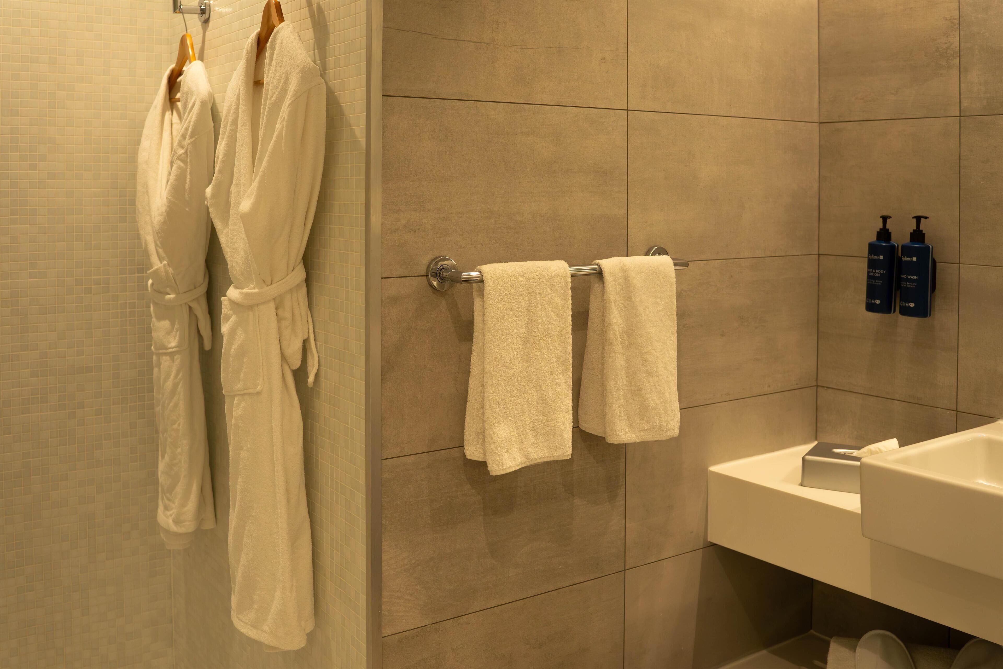 A bathroom with two white towels hanging on a rack, a sink, and two bottles of shampoo and conditioner on the wall.