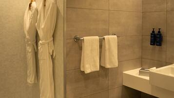 A bathroom with two white towels hanging on a rack, a sink, and two bottles of shampoo and conditioner on the wall.