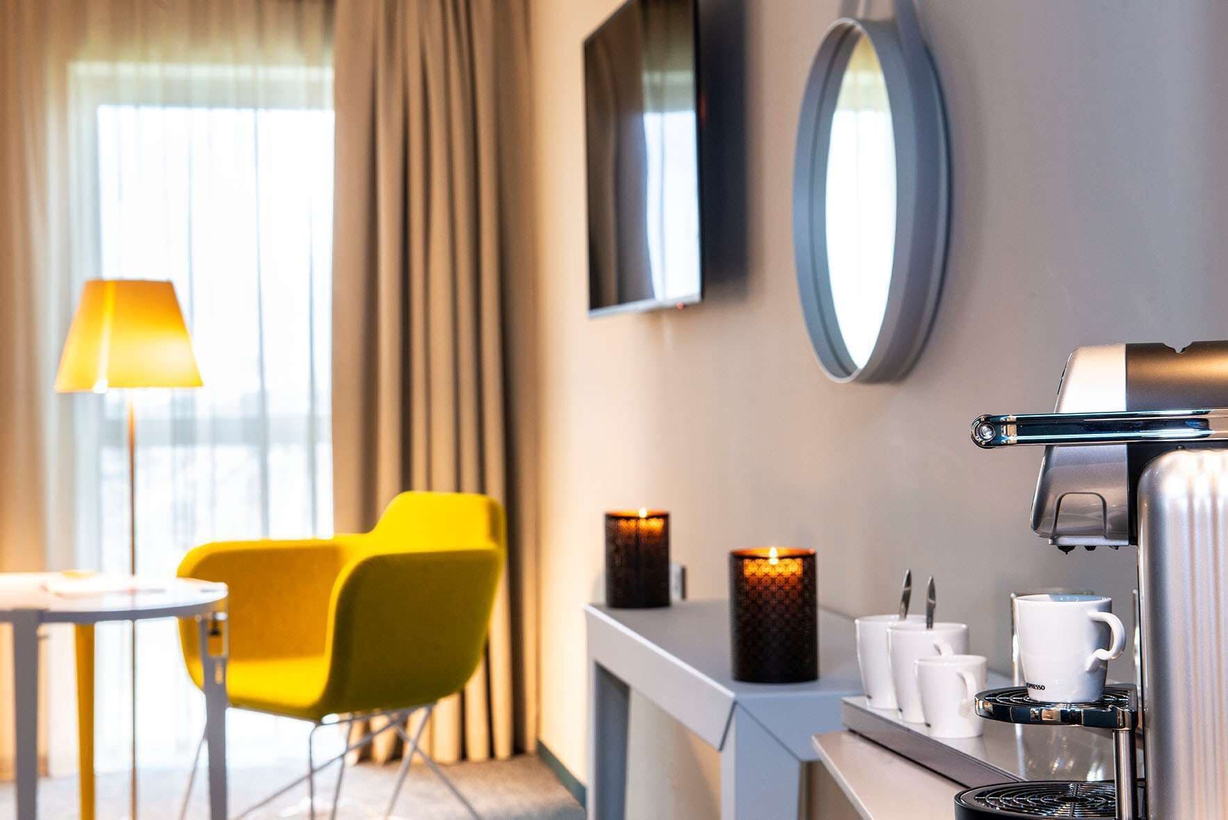 A modern hotel room with a seating area, a coffee machine, and decorative candles.