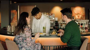 A bar setting with a counter, stools, and a person serving drinks.
