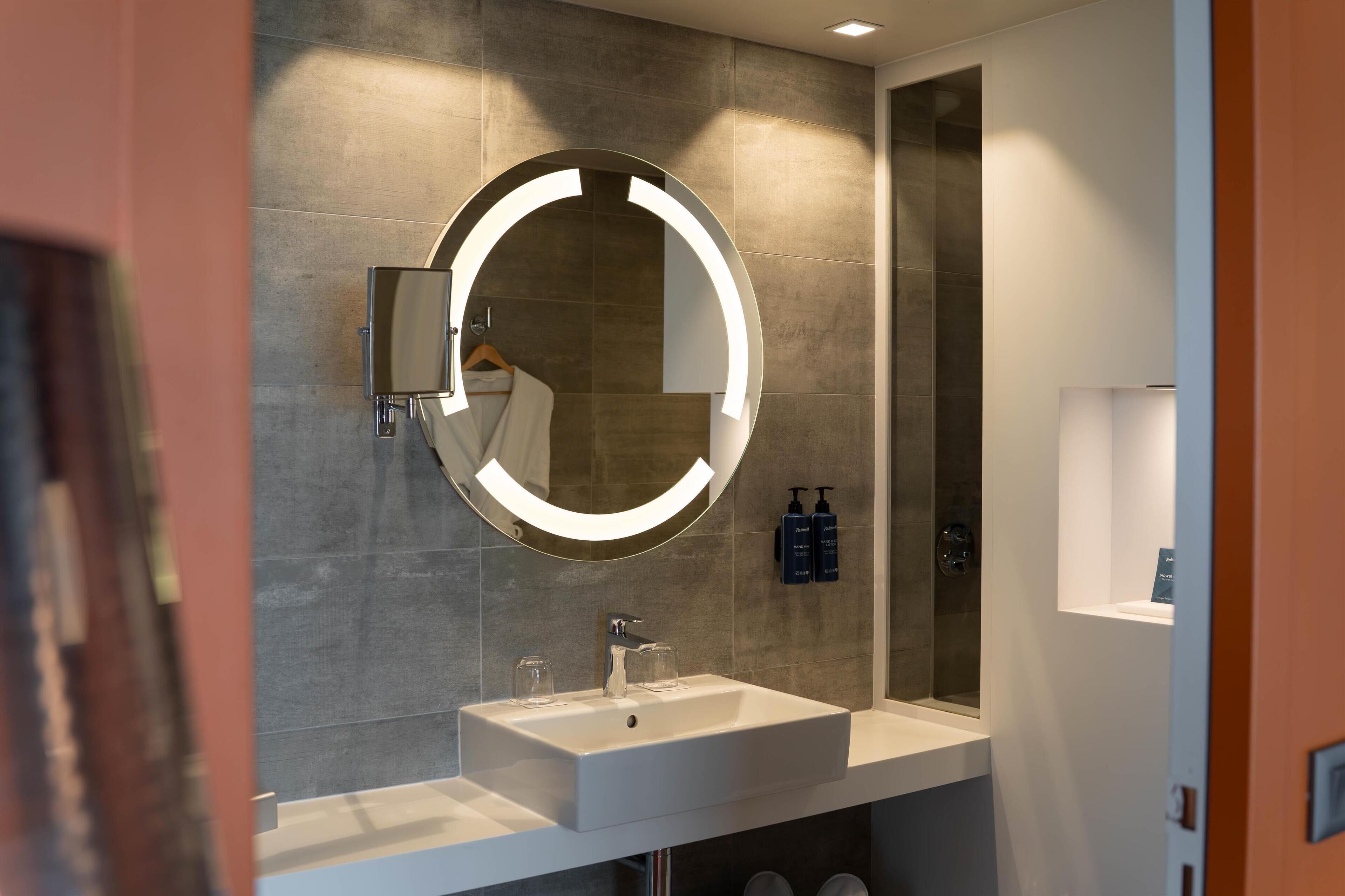 Un baño moderno con un espejo grande, un lavabo y una zona de ducha.