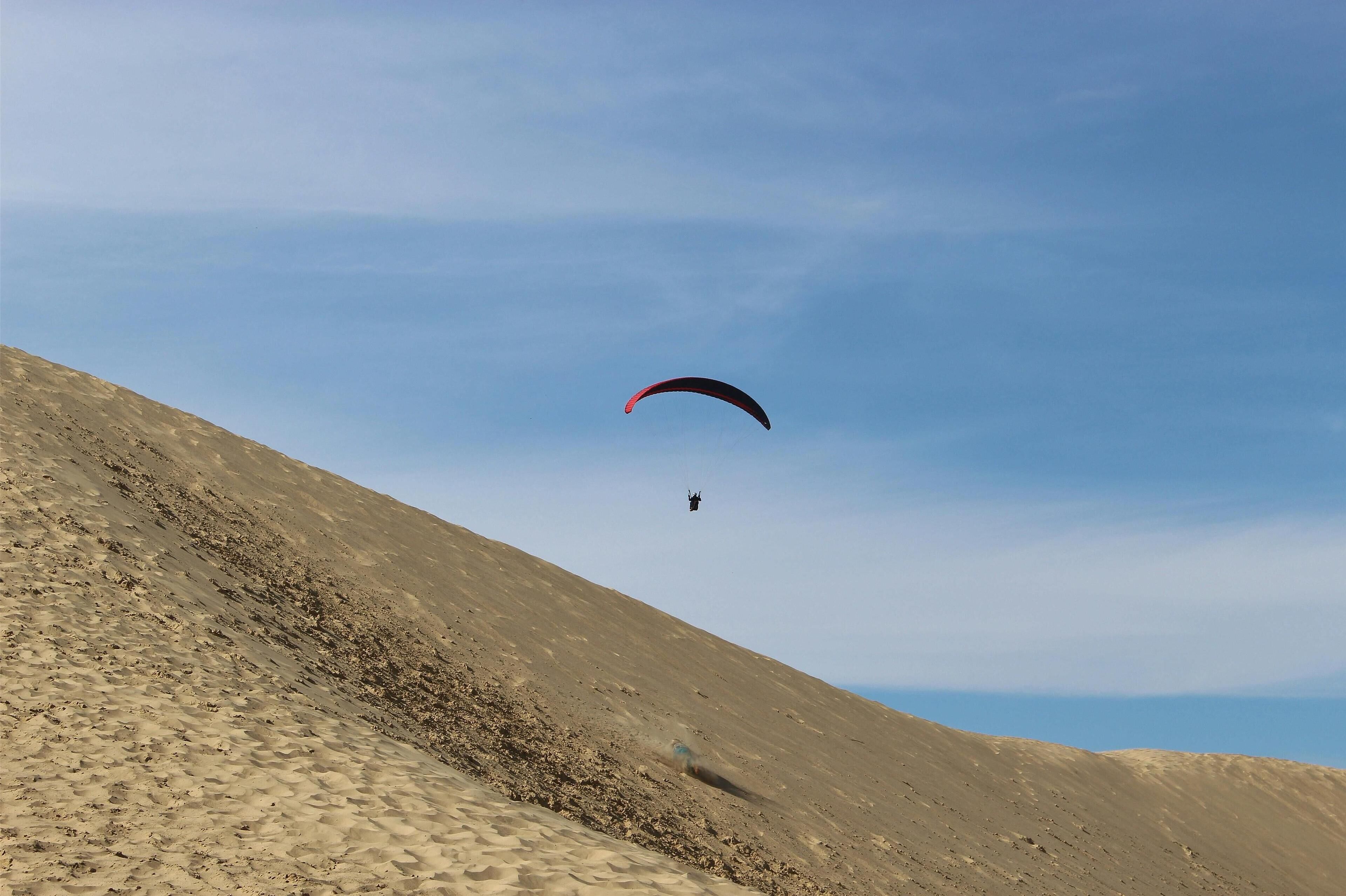 Una persona practica parapente sobre un paisaje desértico.