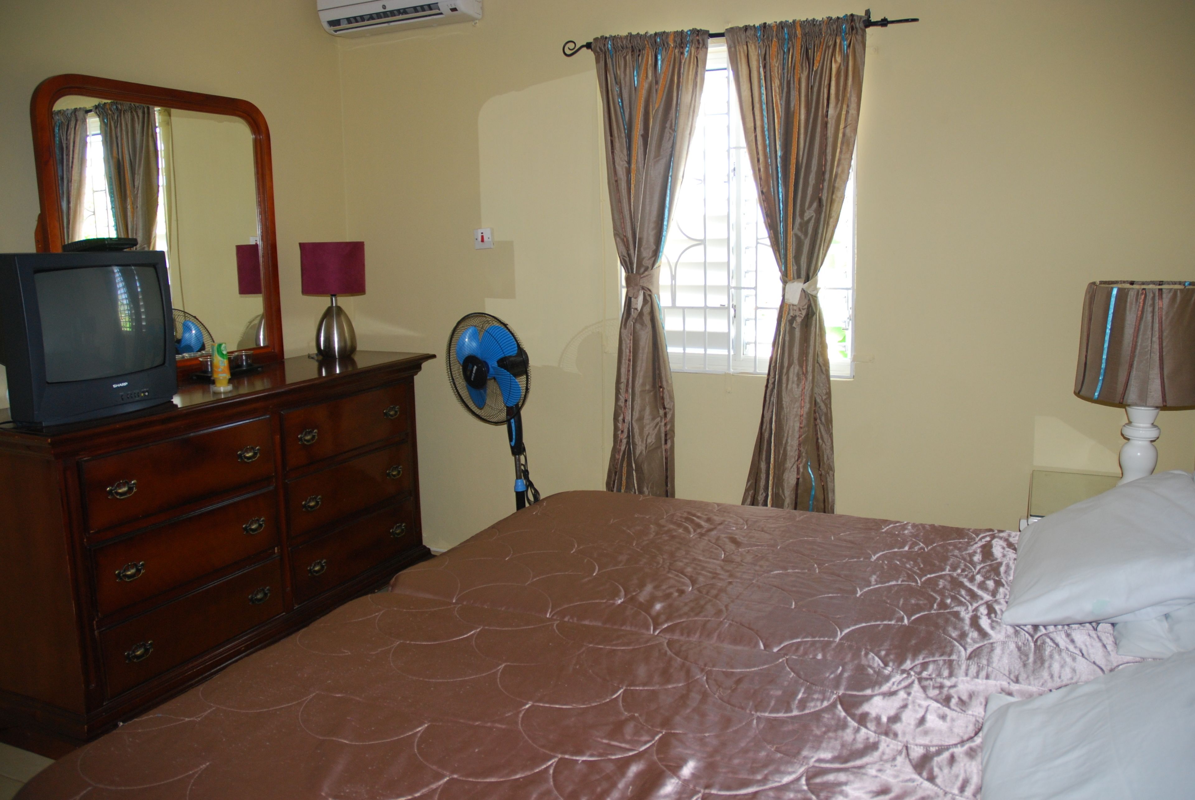 A bedroom with a bed, dresser, mirror, and window with curtains.