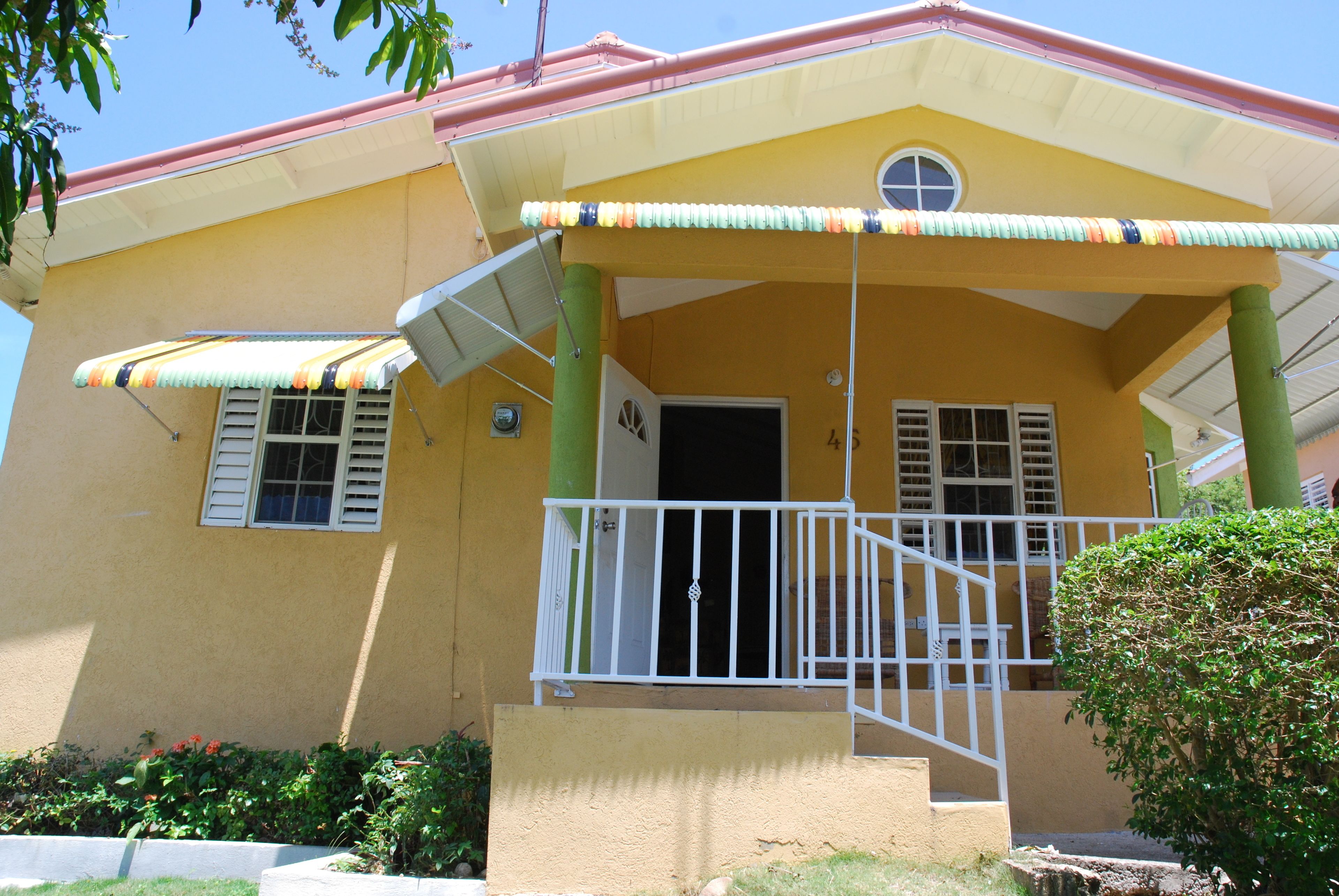A yellow building with a porch, a white railing, and a green column.