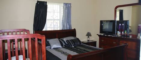 A bedroom with a wooden bed, a television, a dresser, and a window with curtains.