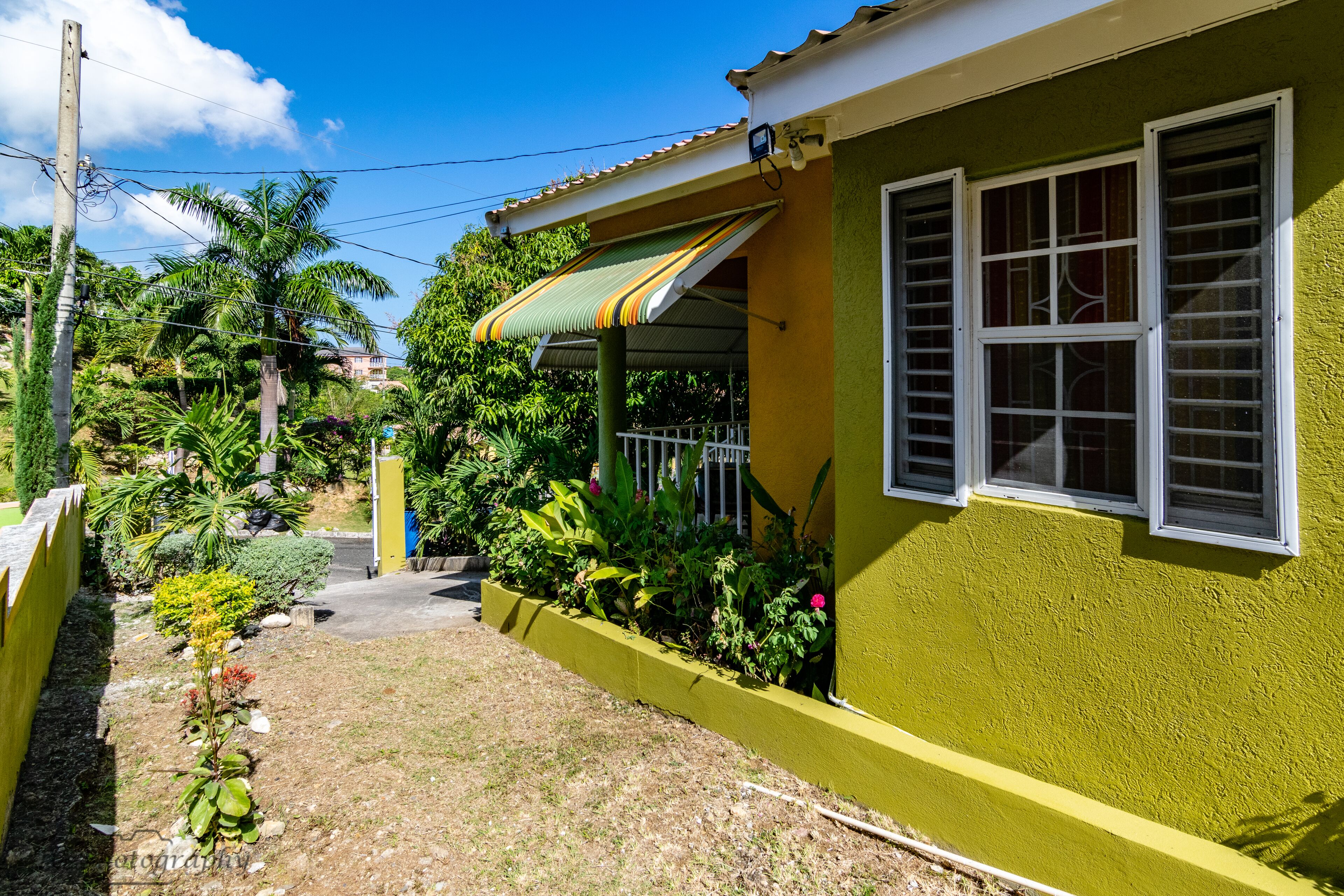 A yellow house with a green awning, a small garden, and a clear blue sky.
