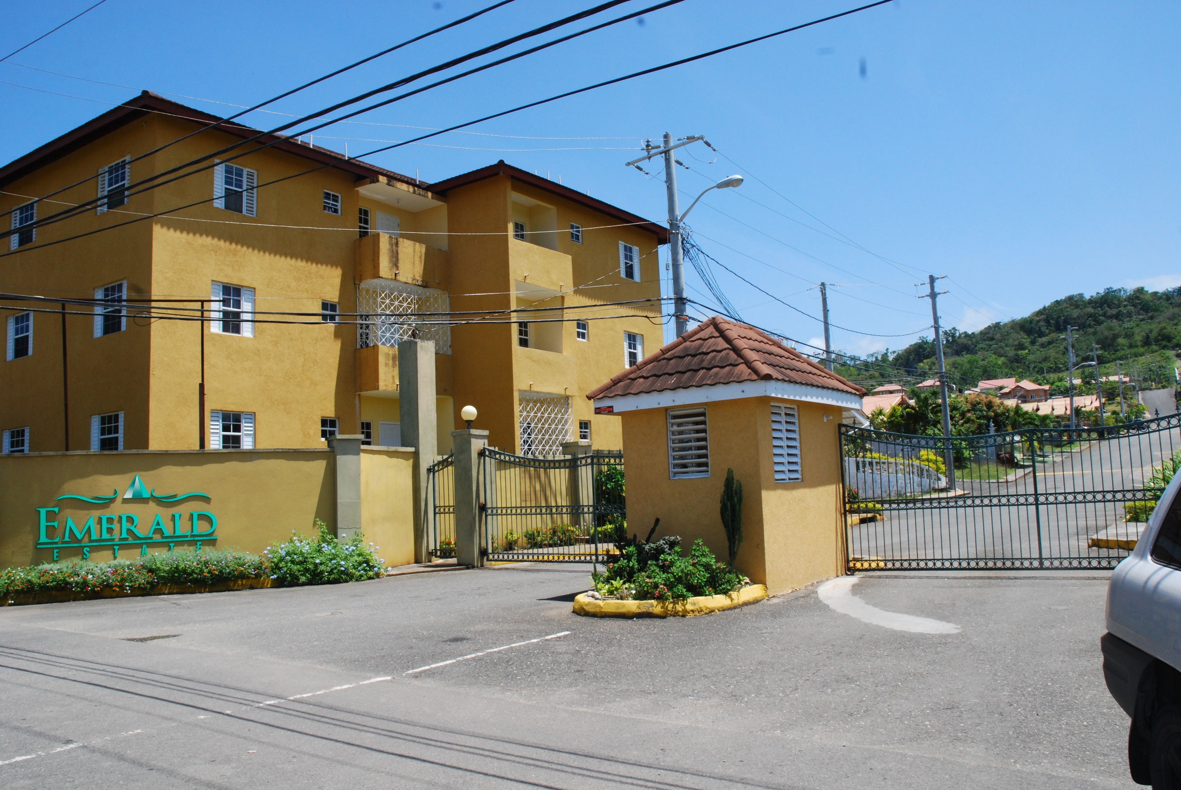 A yellow building with a gated entrance, a small kiosk, and a sign reading "Emerald Estates".