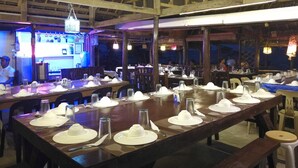 A restaurant with long wooden tables set for dining, a high ceiling with wooden beams, and hanging lights. - Paniman Bay lodge (Caramoan)