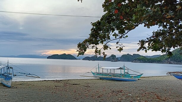 A beach with boats and a clear view of the water and distant mountains. - Paniman Bay lodge (Caramoan)