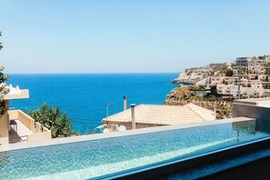 A clear blue sea with a swimming pool in the foreground and buildings in the background.