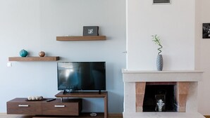 A modern living room with a flat-screen TV on a wooden stand, a fireplace with a vase, and shelves with decorative items. - Steliana 2 (Malevizi)
