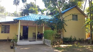 A two-story building with a blue roof and a covered porch. There is a person sitting on the porch. - Nilborno Cottage (Kamalganj)