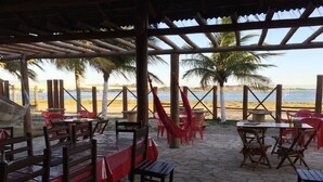 An outdoor patio with stone flooring, wooden tables, and red chairs. - Apto Cabo Frio Marina Clube (Sao Pedro da Aldeia)