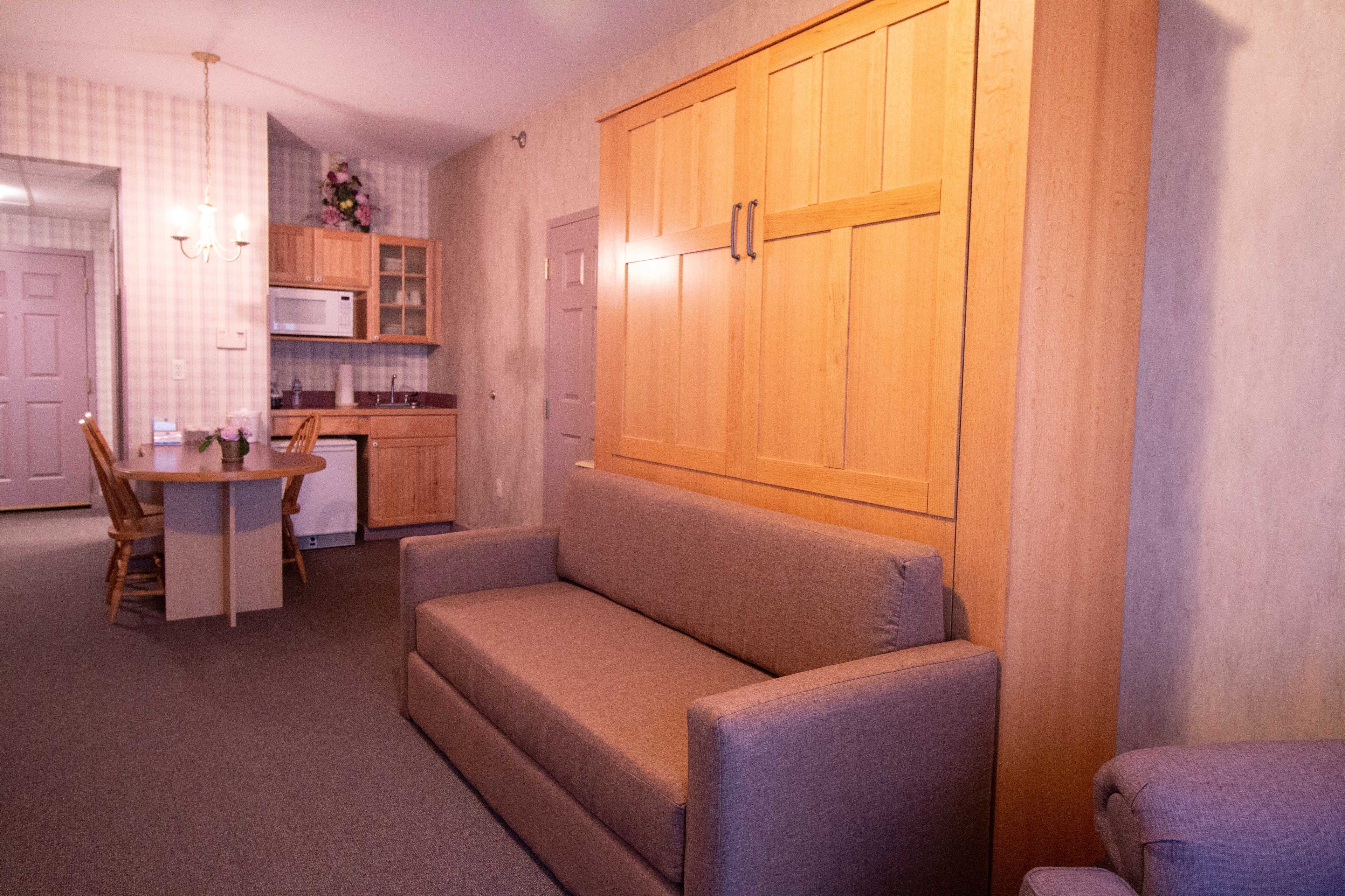 A compact living space with a sofa, a dining table with chairs, a kitchenette, and a wooden wardrobe.