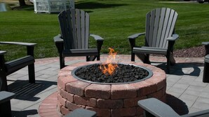 A circular fire pit with chairs around it, set on a brick patio.