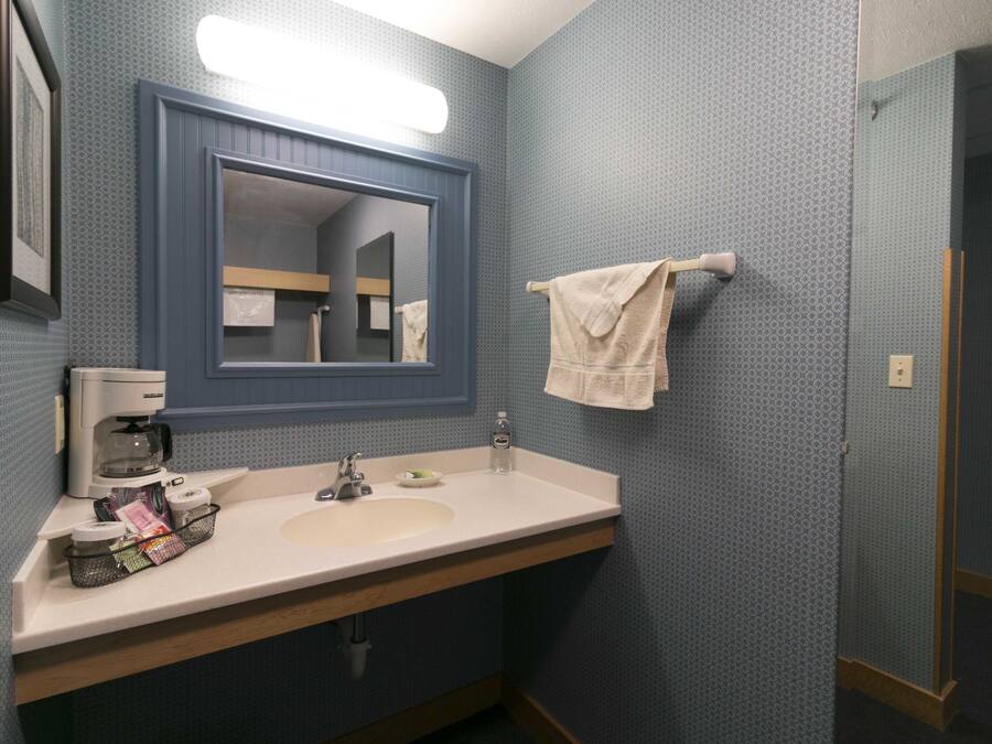 Un baño con lavamanos, espejo, perchero y cafetera.