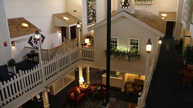 A multi-level hotel interior with a central staircase, a dining area, and a balcony with a white picket fence.