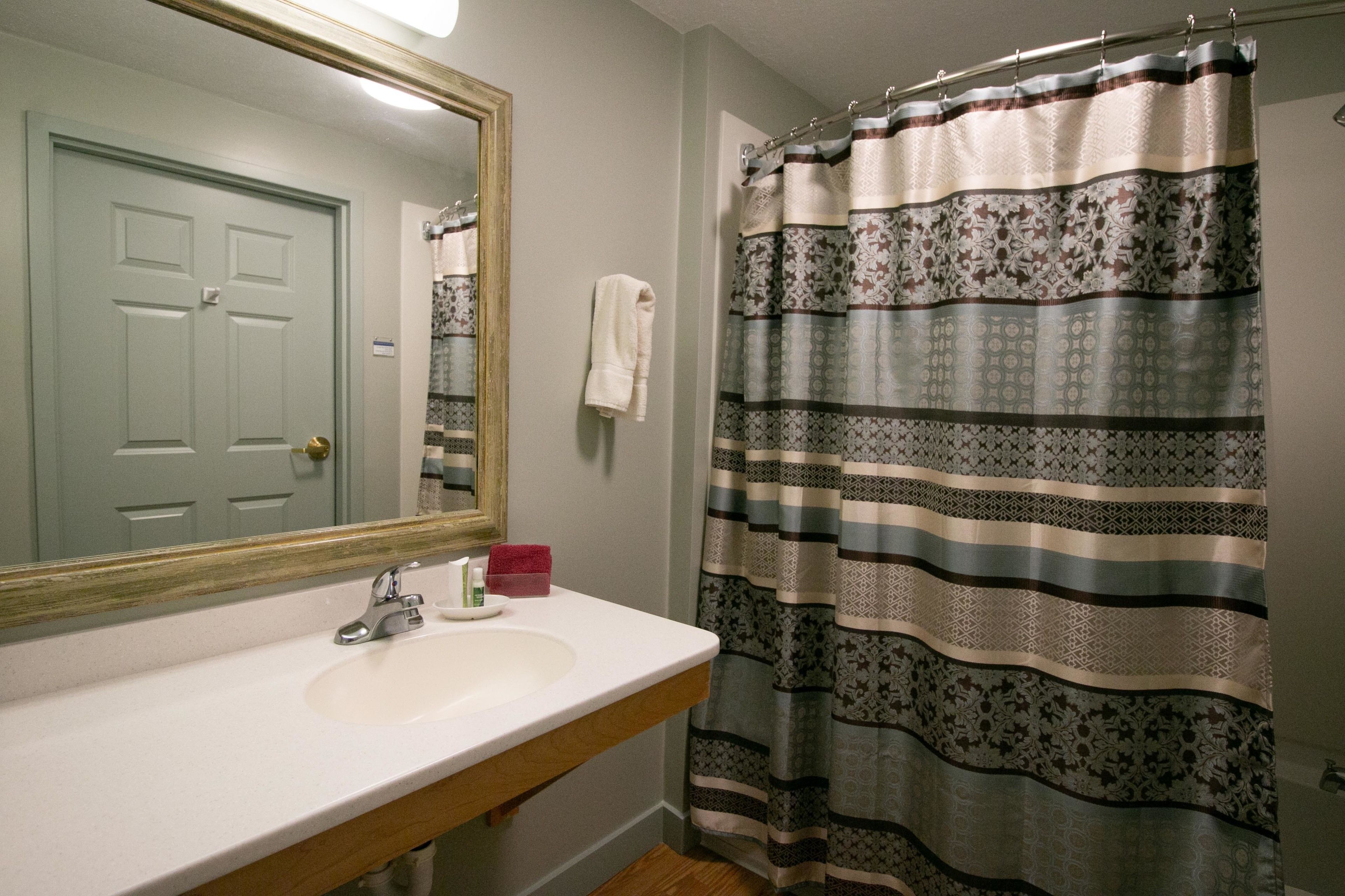 A bathroom with a white sink, a mirror, a door, and a patterned shower curtain.