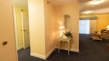 A hotel hallway with a carpeted floor, a small table with a lamp and a plant, and a door leading to another room.