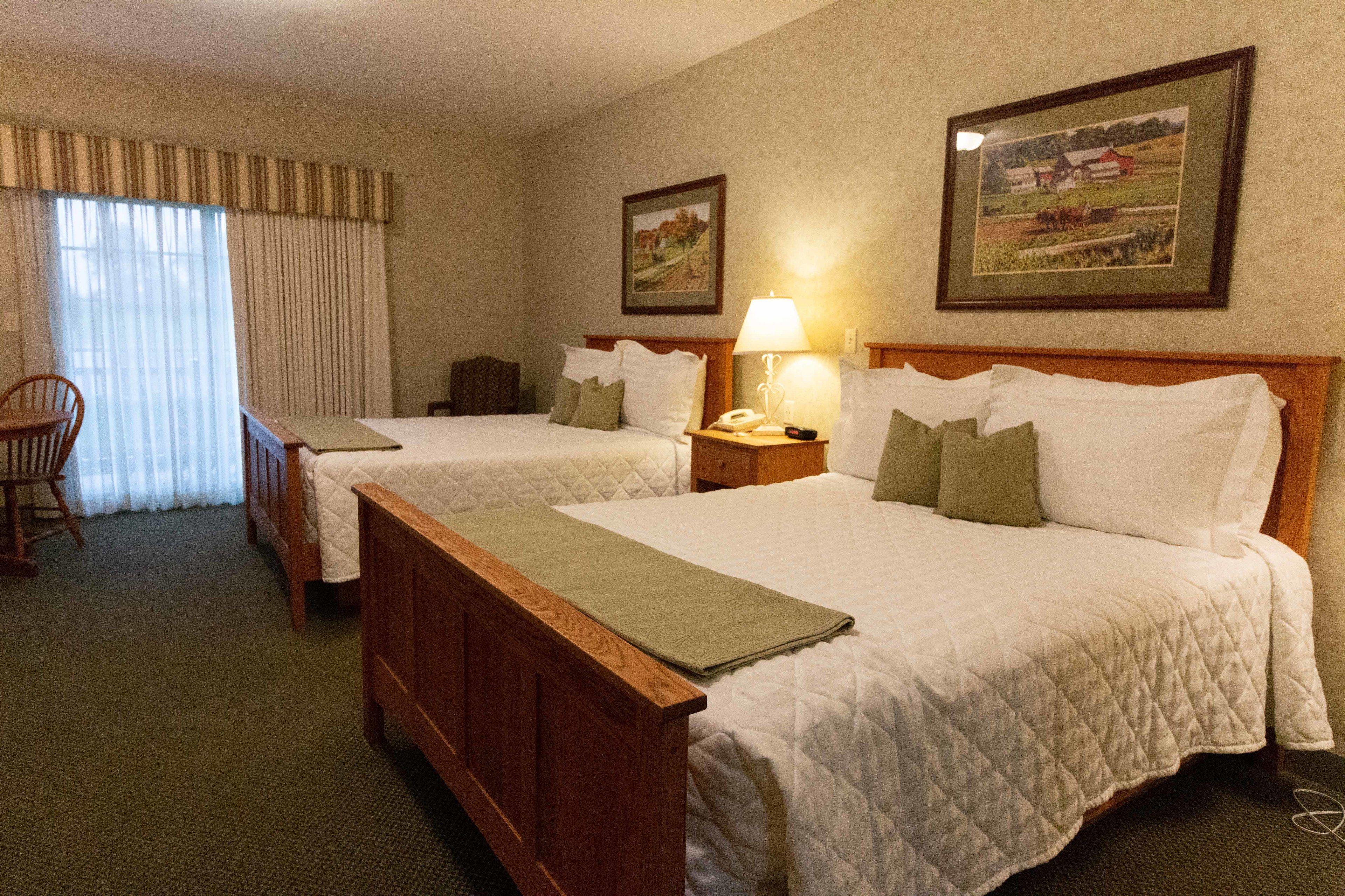 A hotel room with two beds, a chair, a nightstand with a lamp, and framed pictures on the wall.