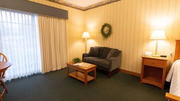 Une chambre d’hôtel avec un canapé, une petite table, une lampe, une table de chevet en bois et une chaise.