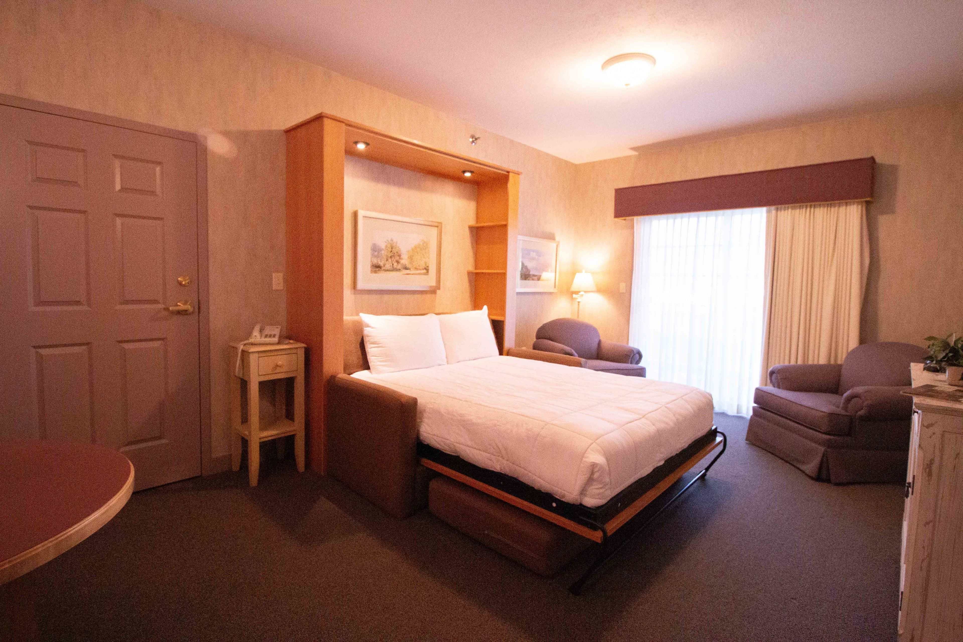 A hotel room with a bed, a chair, a desk, and a window with curtains.