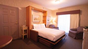 Quarto de hotel com cama, uma cadeira, escrivaninha e janela com cortinas.