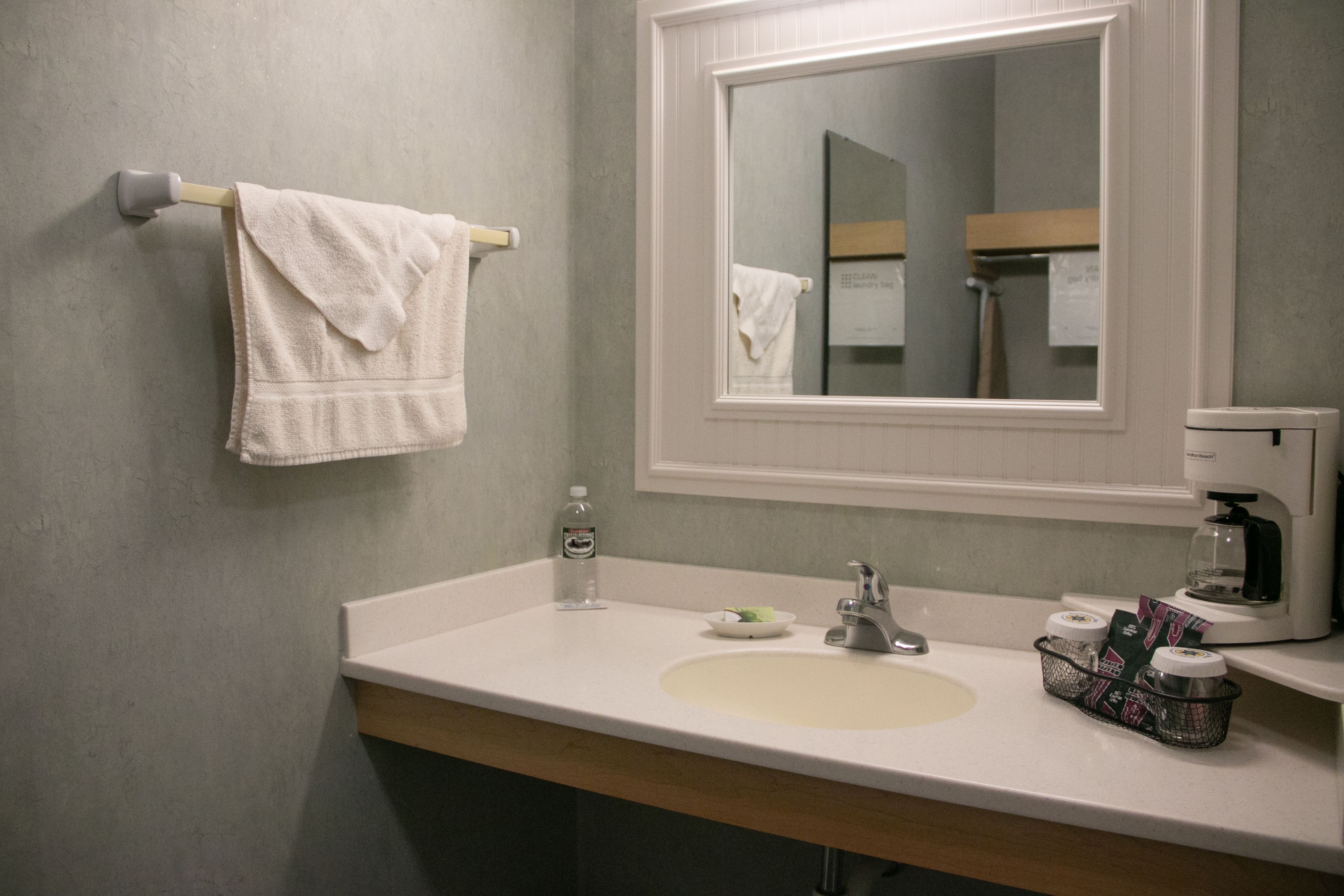 Ein Badezimmer mit Waschbecken, Spiegel, Handtuchhalter und einer Kaffeemaschine.