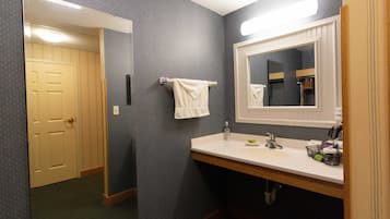 A bathroom with a sink, mirror, towel rack, and a door leading to another room.