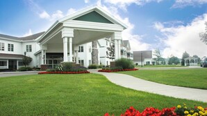 A large, white building with a covered entrance and a well-maintained lawn with red and yellow flowers.