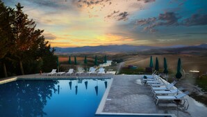 A poolside area with lounge chairs and umbrellas, surrounded by trees and a view of distant hills. - Glamping Diacceroni (Peccioli)