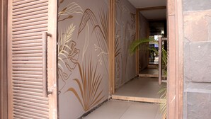 A hallway with a beige wall featuring a floral pattern, a wooden door, and a stone wall on the right. - Hotel Natural (Medellín)