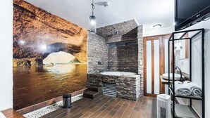 A modern bathroom with a stone wall, a built-in bathtub, and a large mural of a cave. - Hotel Natural (Medellín)