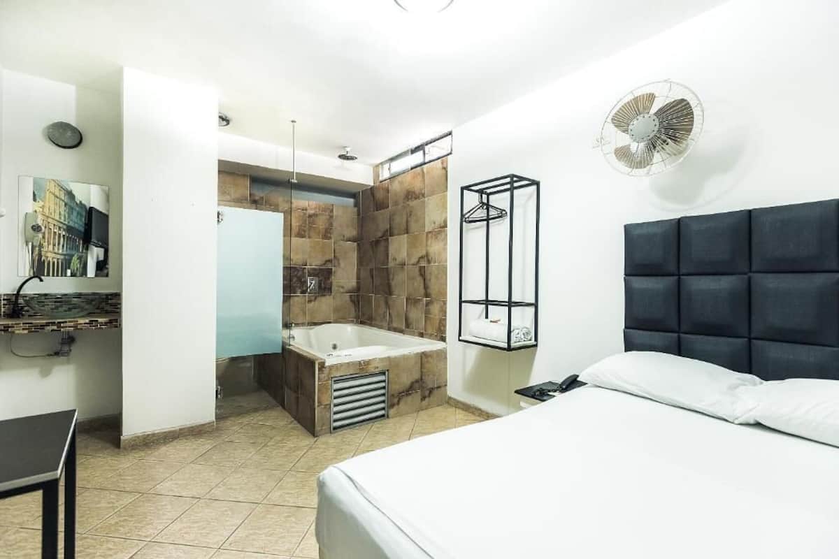 A modern hotel room with a large bed, a built-in bathtub, a shower area, and a small table.