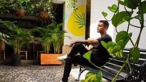 A man sitting on a bench in a room with potted plants and a yellow wall. - Hotel Natural (Medellín)