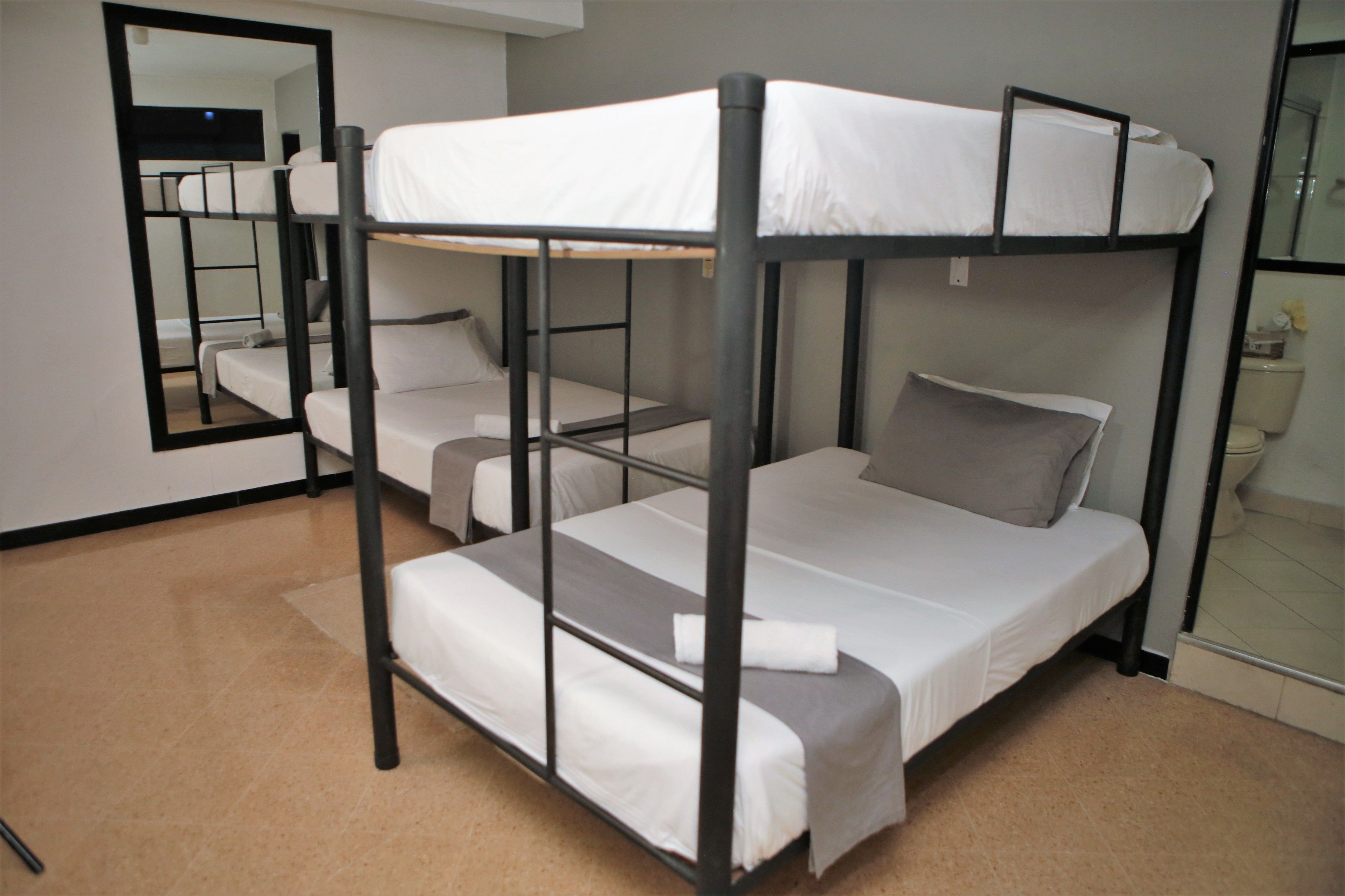 A bunk bed room with a mirror on the wall, a small window, and a toilet visible in the corner.